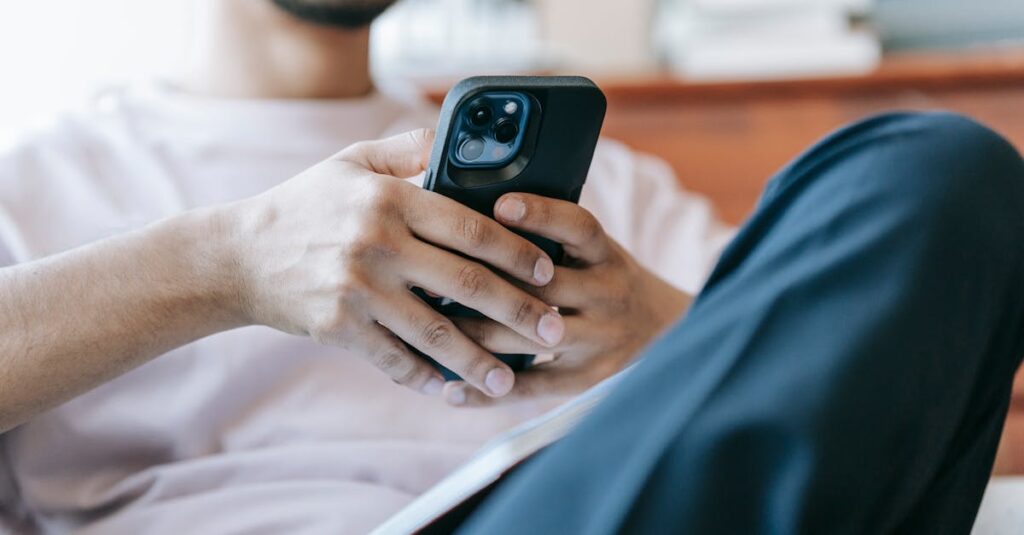 Crop bearded male in casual clothes browsing mobile phone and sitting in light living room