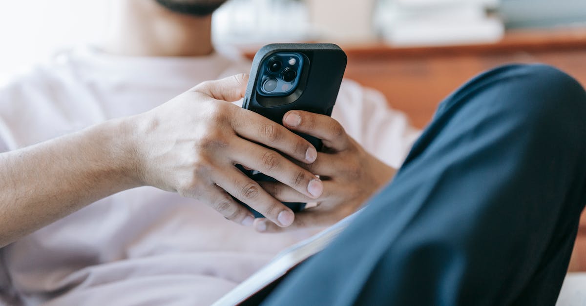 Crop bearded male in casual clothes browsing mobile phone and sitting in light living room